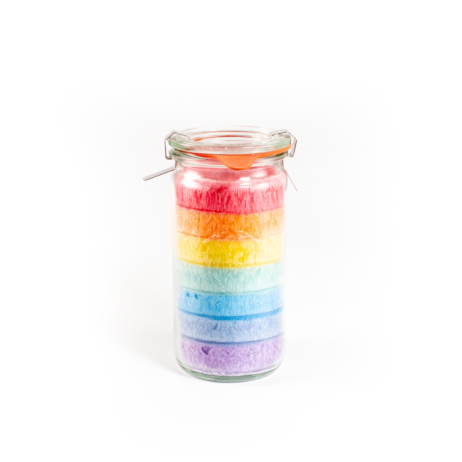 Kristallkerze in einem schlanken, runden, hohen und durchsichtigem Einmachglas. Das Wachs ist wie ein Regenbogen von unten nach oben in den Farben violett, dunkelblau, hellblau, hellgrün, gelb, orange, rot geschichtet