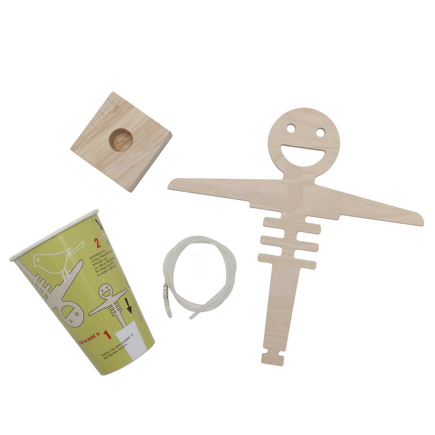 Ein Bauset für einen „Bungeejumper“ zur Fütterung von Wildvögeln. Es besteht aus einer lachenden Holzfigur, einem Holzwürfel mit Vertiefung, einer Schnur und einem grünen Becher mit Aufbauanleitung.