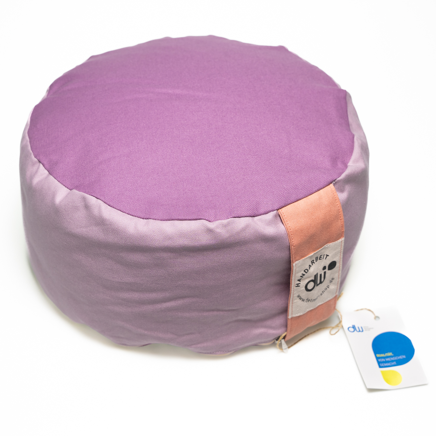 Rundes Yogasitzkissen. Die Seite ist lila oben und unten ist der Stoff fliederfarben. An der Seite ist eine Stofflasche in der Farbe rosé zum Tragen und der Bezug kann mit einem Reißverschluss geöffnet werden.