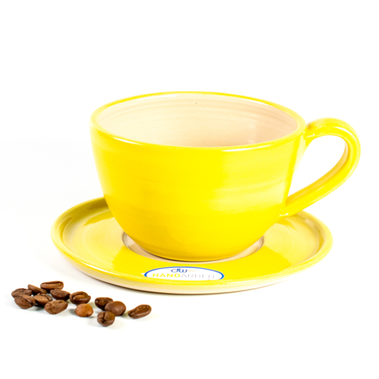 Eine gelbe leicht durchscheinend glasierte Cappuccino Tasse auf einer Untertasse, mit gleichfarbigem Rand. Das innere der Tasse und Untertasse ist in ein naturbelassenes helles Beige. Daneben liegen ein paar Kaffeebohnen.