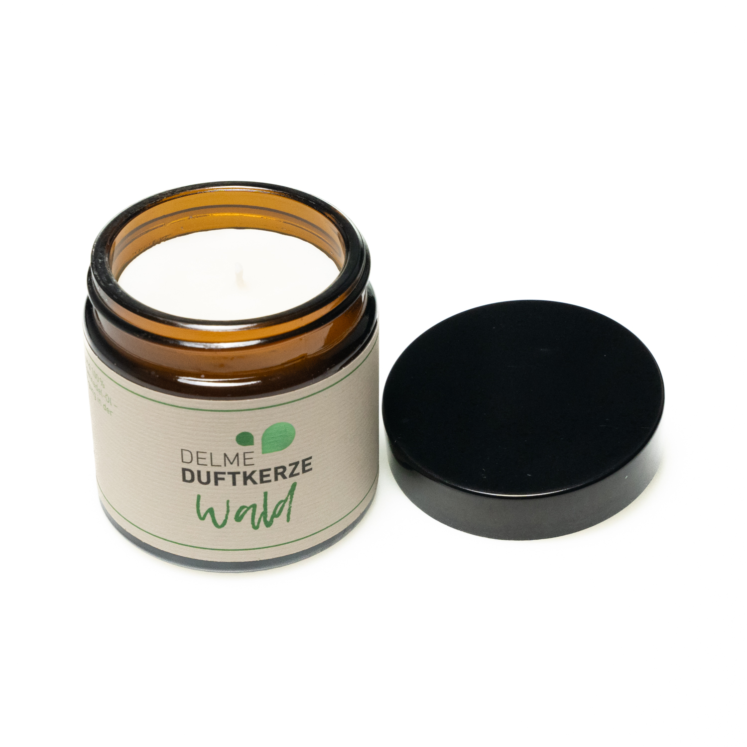 Kleines rundes dunkelbraunes Glas mit schwarzem Deckel und cremeweißem Etikett mit dezenter grüner Aufschrift. Das Wachs der Kerze ist weiß.