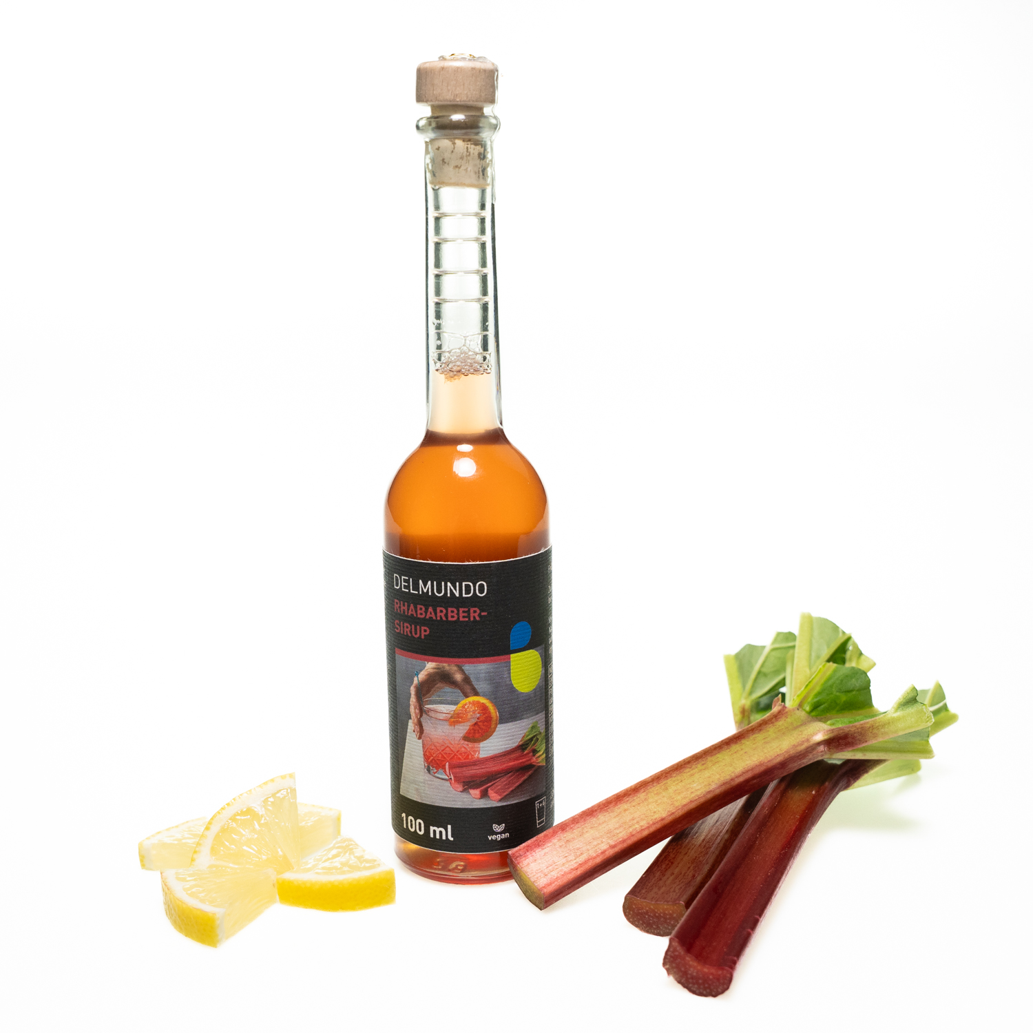 Eine klare Glasflasche mit Bügel-Verschluss gefüllt mit tiefrotem Rhabarbersirup. Daneben liegen Rhabarberstücke und ganze Rhabarberstangen.