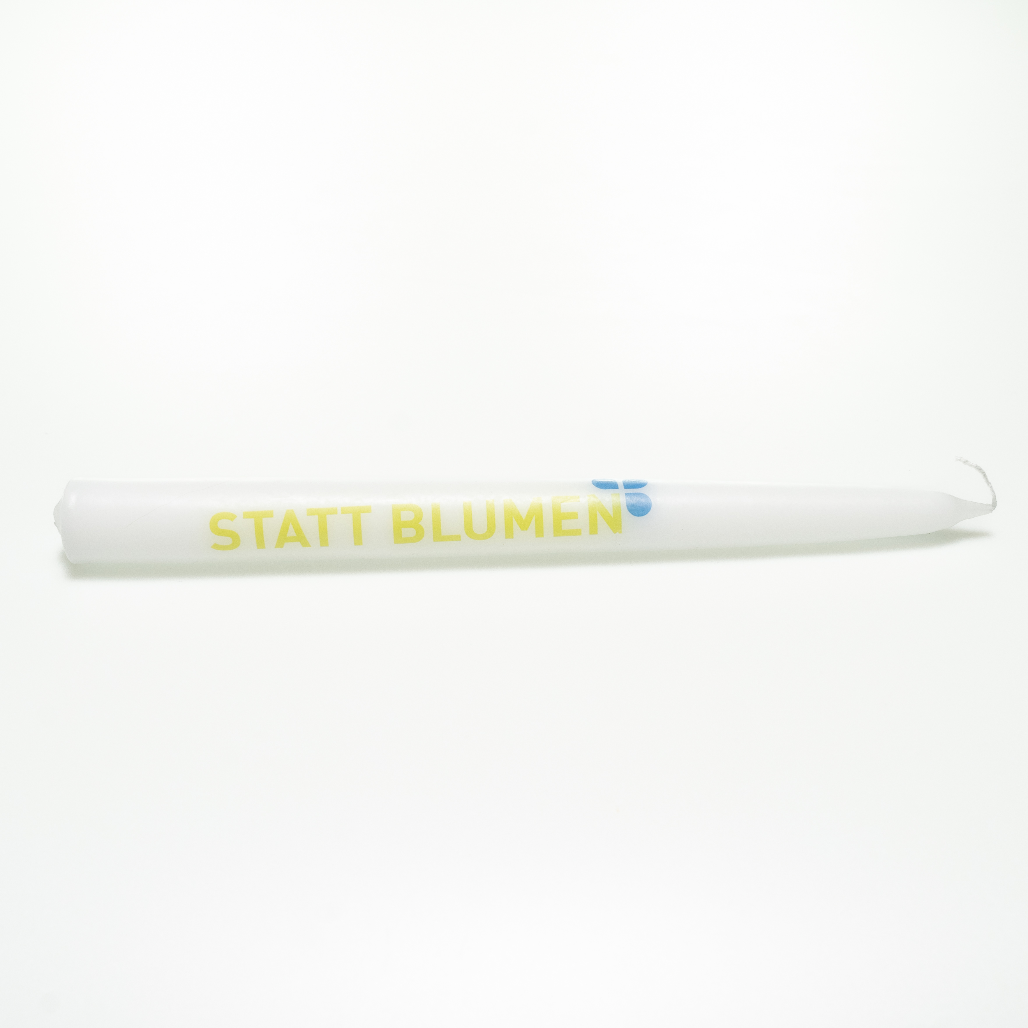 Weiße Tafelkerze mit der Aufschrift „Statt Blumen“ in hellgrünen, fetten, schlichten Versalien. Oben um das „N“ sind drei Blaue Tropfen wie ein Kleeblatt angeordnet.