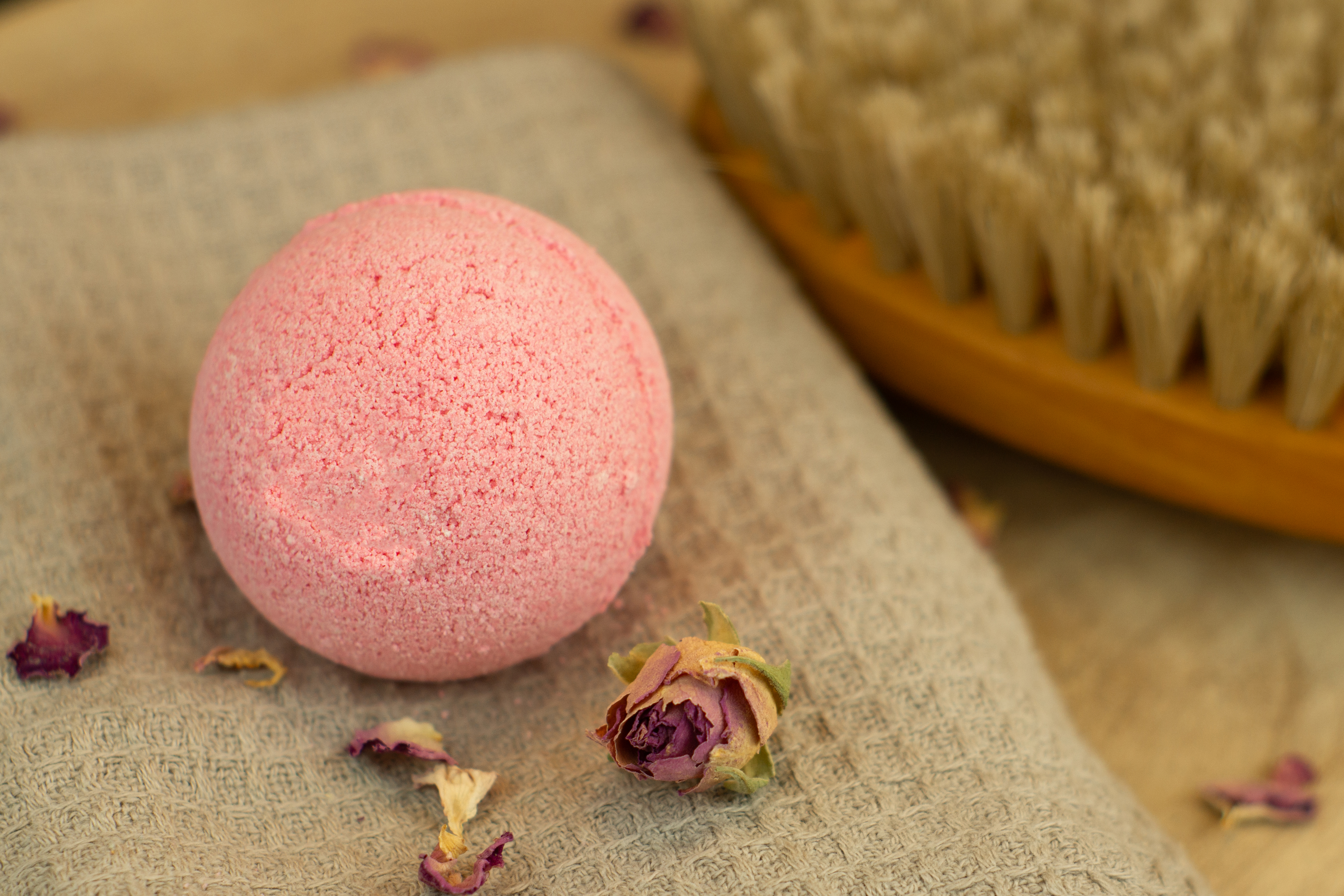 Hellrosane Badekugel auf einem Handtuch mit Rosenblüten