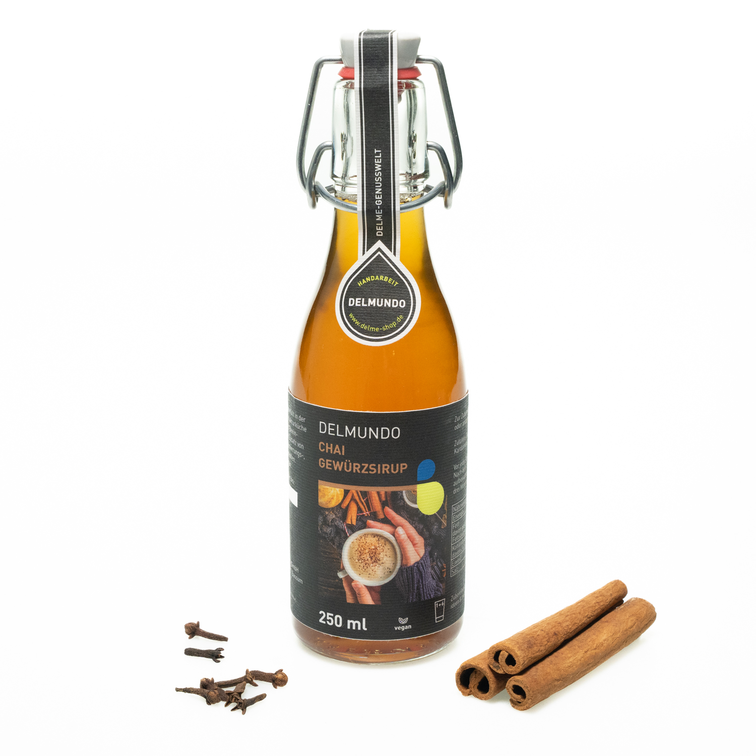 Eine klare Glasflasche mit Bügel-Verschluss gefüllt mit goldbraunem Gewürzsirup. Daneben liegen Zimtstangen und Gewürznelken.
