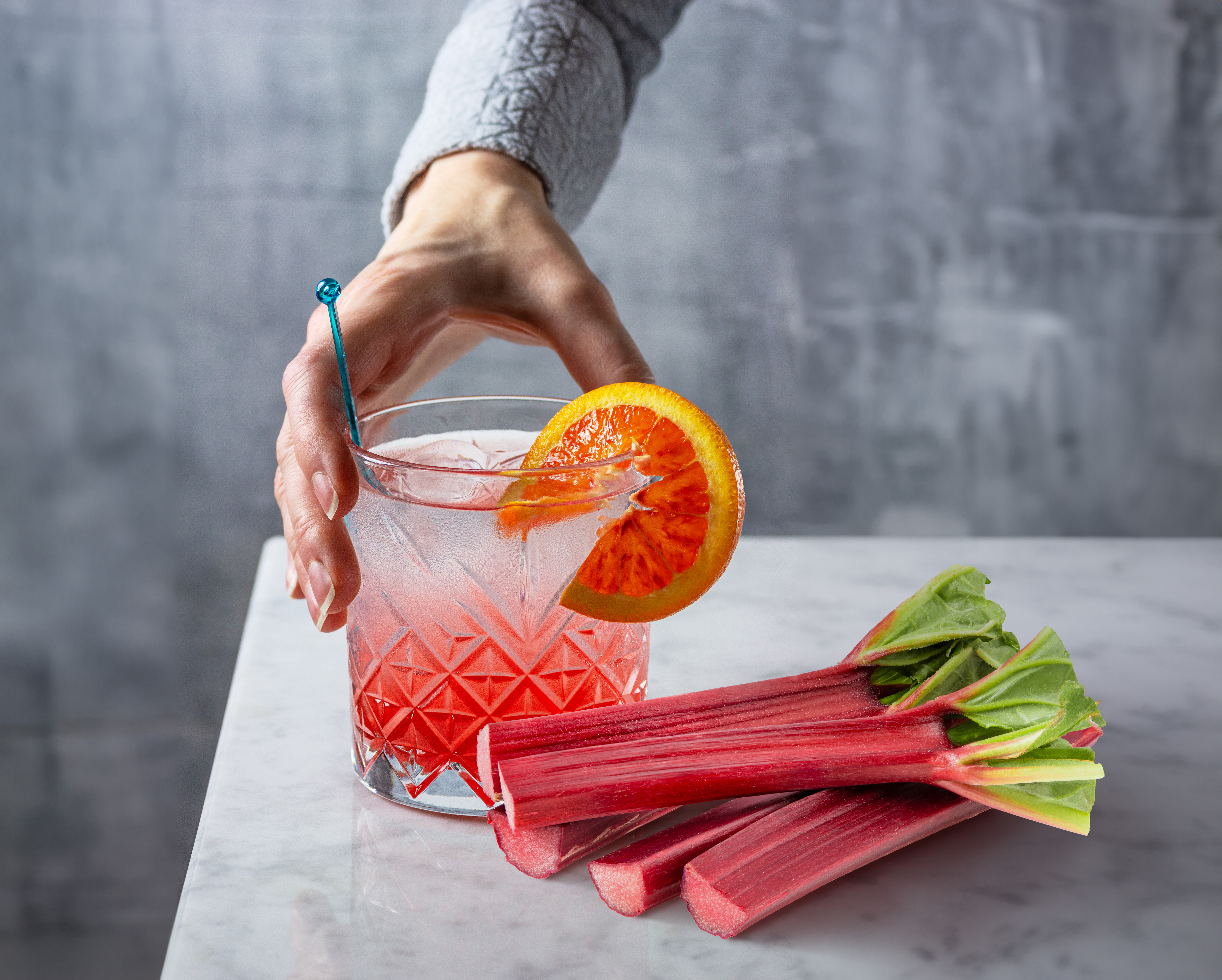Ein Rhabarbercocktail mit frischen Rhabarberstangen daneben