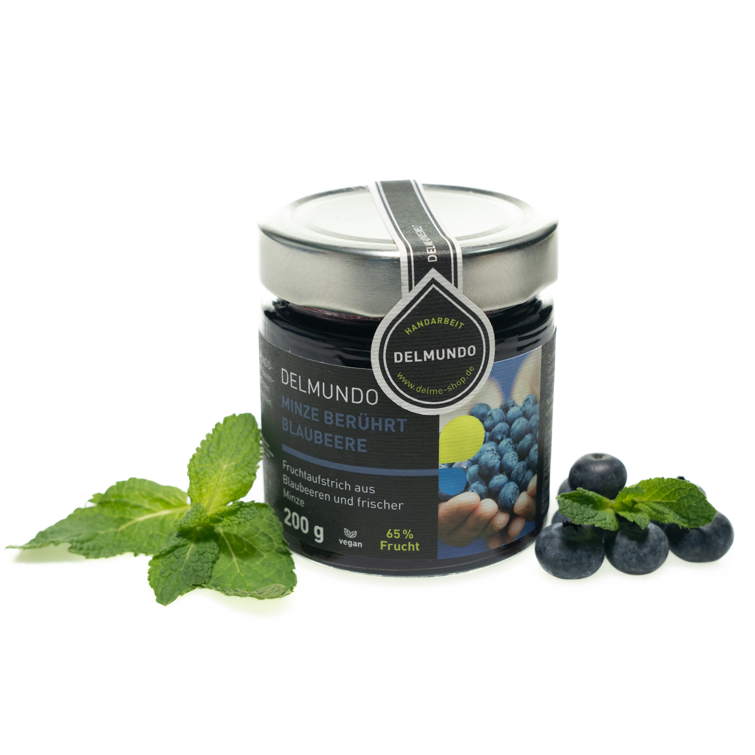 Rundes Glas mit silbernem Deckel, gefüllt mit dunkelblauem Fruchtaufstrich. Daneben liegen ein paar Minzblätter und Blaubeeren.